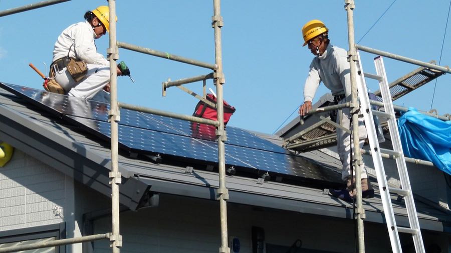 Installers fitting solar panels on a house roof (openly-licensed stand-in photo)